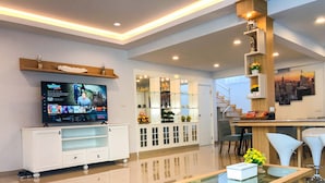 A modern living room with a flat-screen TV, a sofa, a coffee table, and a dining area with chairs and a table. - Gala Express (Pattaya)