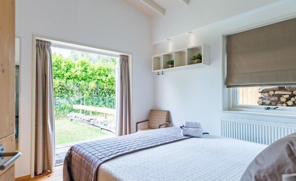A bedroom with a large bed, a chair, a window with a view of greenery, and a built-in shelf with plants.
