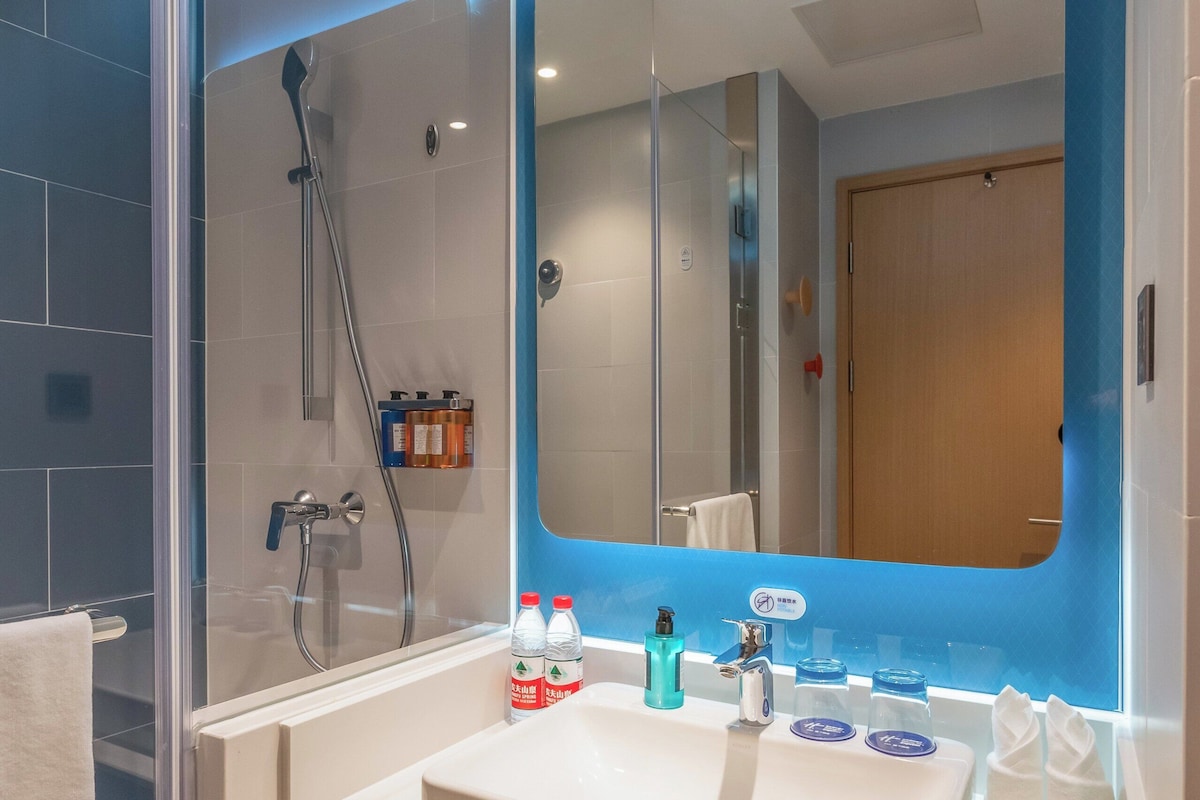 A modern bathroom with a glass-enclosed shower, a white sink with blue soap dispensers, and a large mirror with a blue accent.