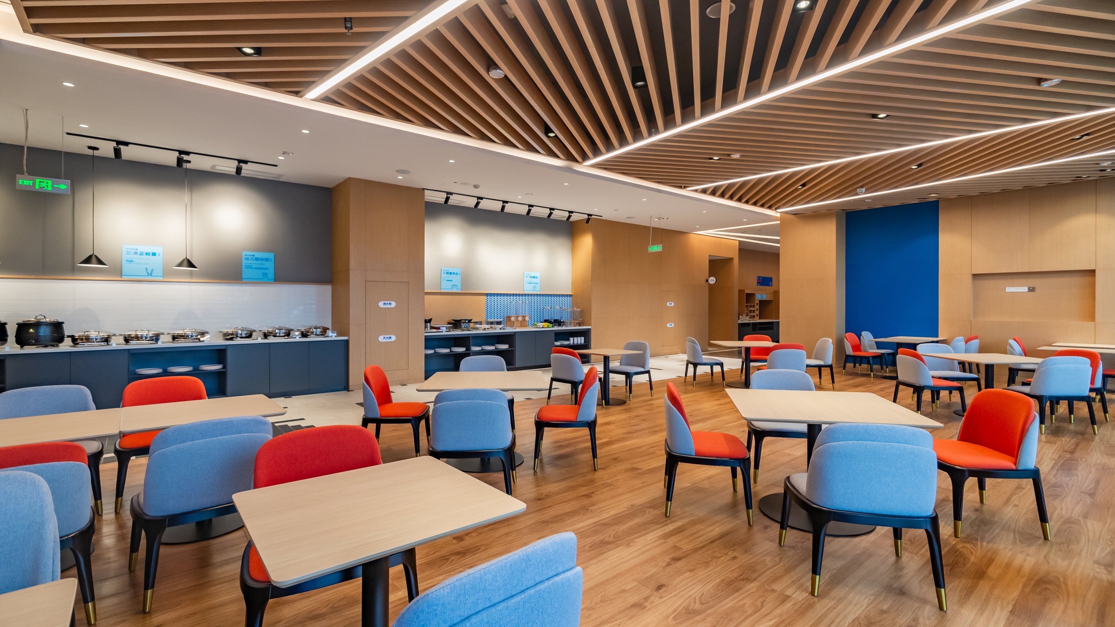 Un comedor moderno con varias mesas y sillas, una zona de cocina con equipo de cocina, y una pared azul de acento.