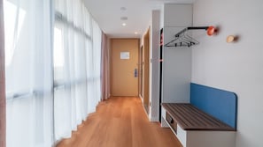 A hotel hallway with a wooden floor, a bench, a coat rack, and a door with a sign.