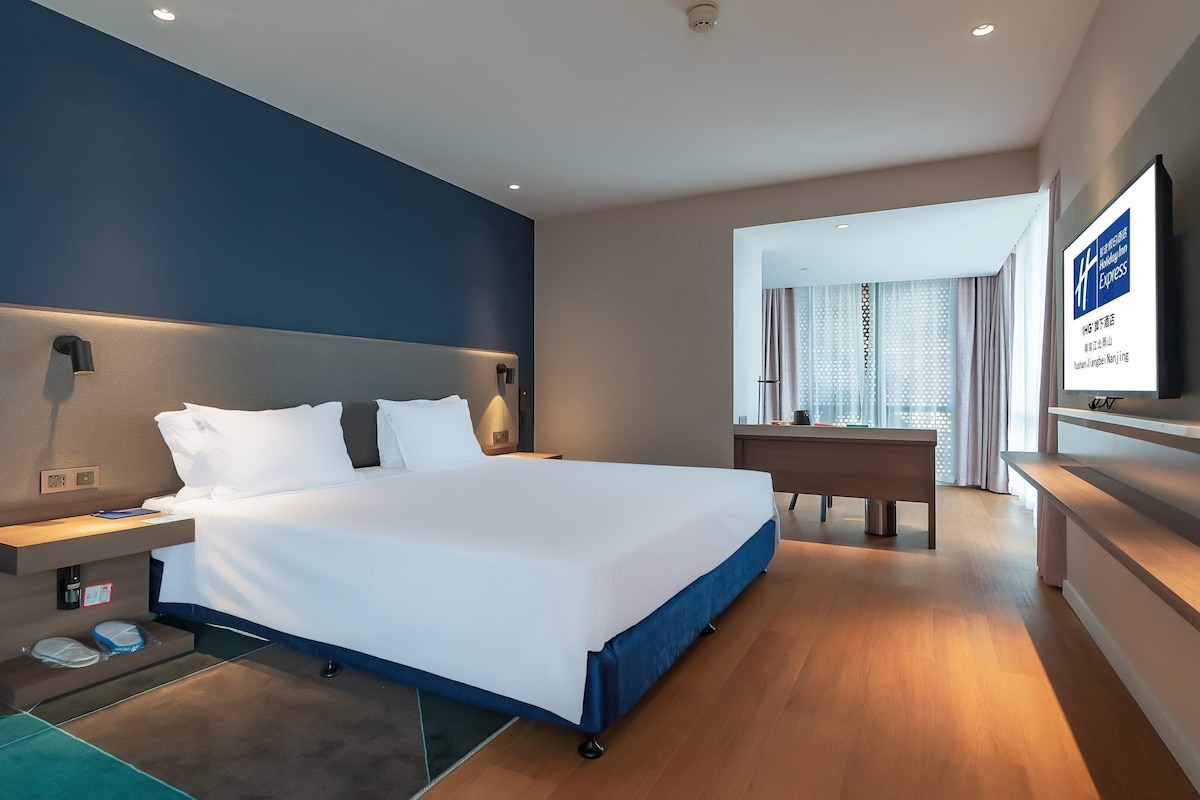 A modern hotel room with a large bed, bedside tables, a desk, and a television.