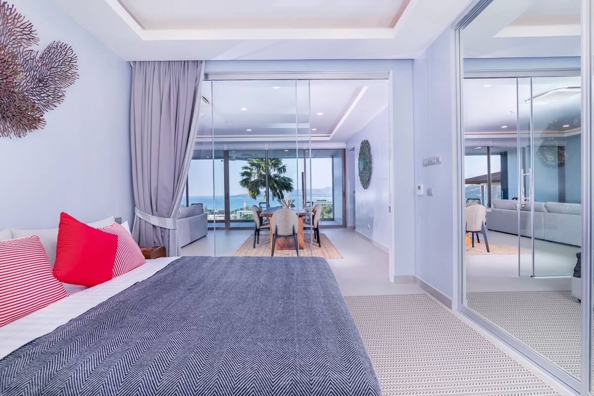A modern bedroom with a large bed, a dining area with a view, and a sliding glass door leading to a balcony.