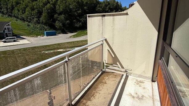 A balcony with a metal railing overlooking a parking area and a building with a sloped roof.