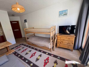 Uma cama beliche com uma televisão e uma cômoda de madeira em um quarto com tapete estampado.