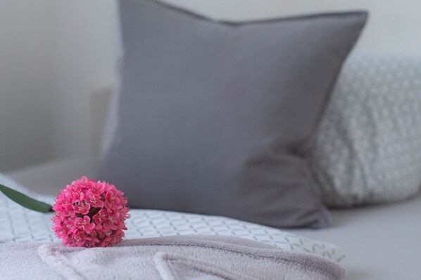 A bed with a grey pillow, a white pillow, and a pink flower on a white blanket. - Hotel Schenk (Pirmasens)