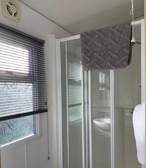 Ein Badezimmer mit Dusche, einem Fenster mit Jalousien und einem Handtuch an der Wand.