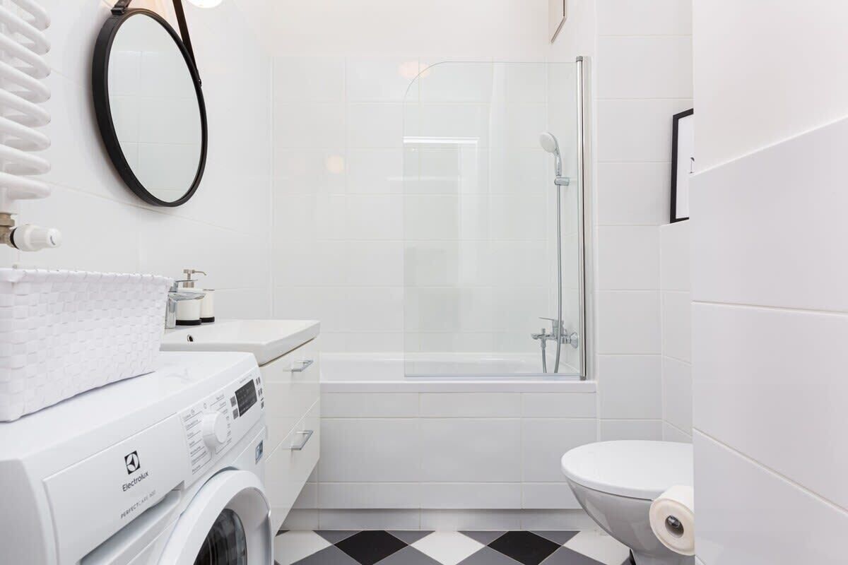 A modern bathroom with a washing machine, a glass-enclosed shower, and a toilet.
