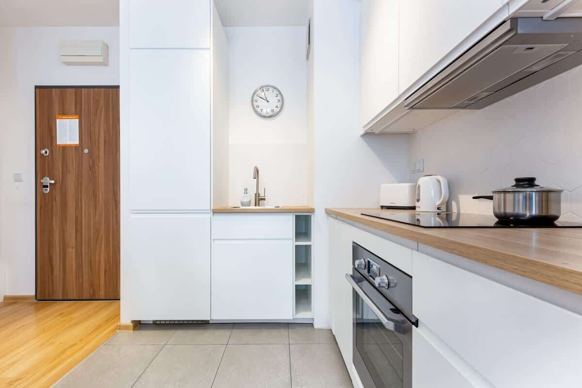 Una cocina moderna con armarios blancos, una puerta de madera, un reloj y una estufa.