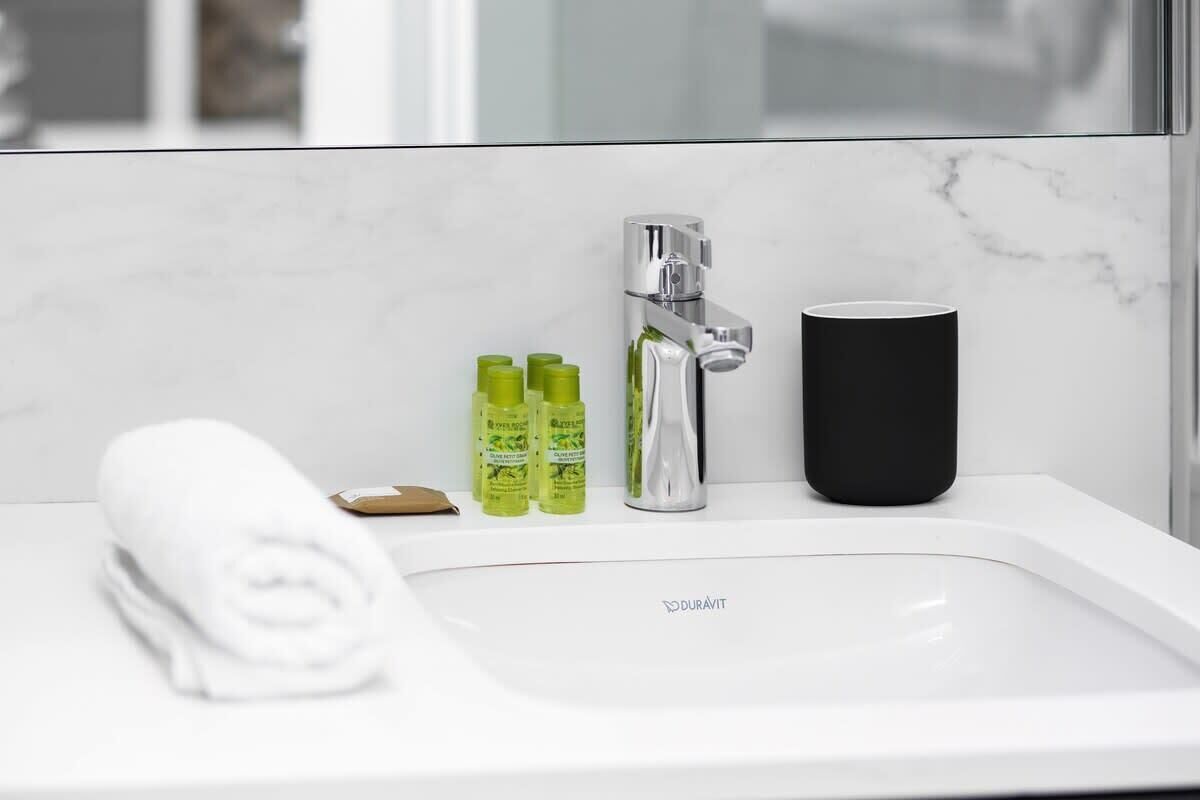 Ein modernes Badezimmer mit einem weißen Waschbecken, einem Chrom-Wasserhahn und drei grünen Seifenspendern.