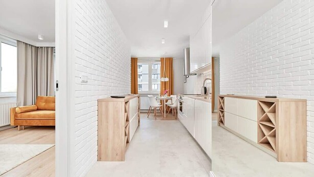 A modern kitchen with white brick walls, wooden cabinetry, and a dining area with a table and chairs.