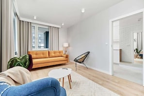 A modern living room with a sofa, a chair, a small table, and a view of a kitchen area.
