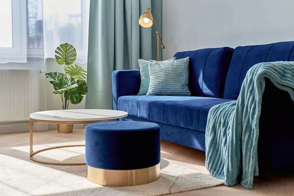 A modern living room with a blue sofa, a round coffee table, a floor lamp, and a potted plant.