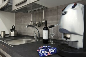 Uma cozinha com uma pia de aço inoxidável, uma chaleira, uma garrafa de vinho e uma máquina de café.