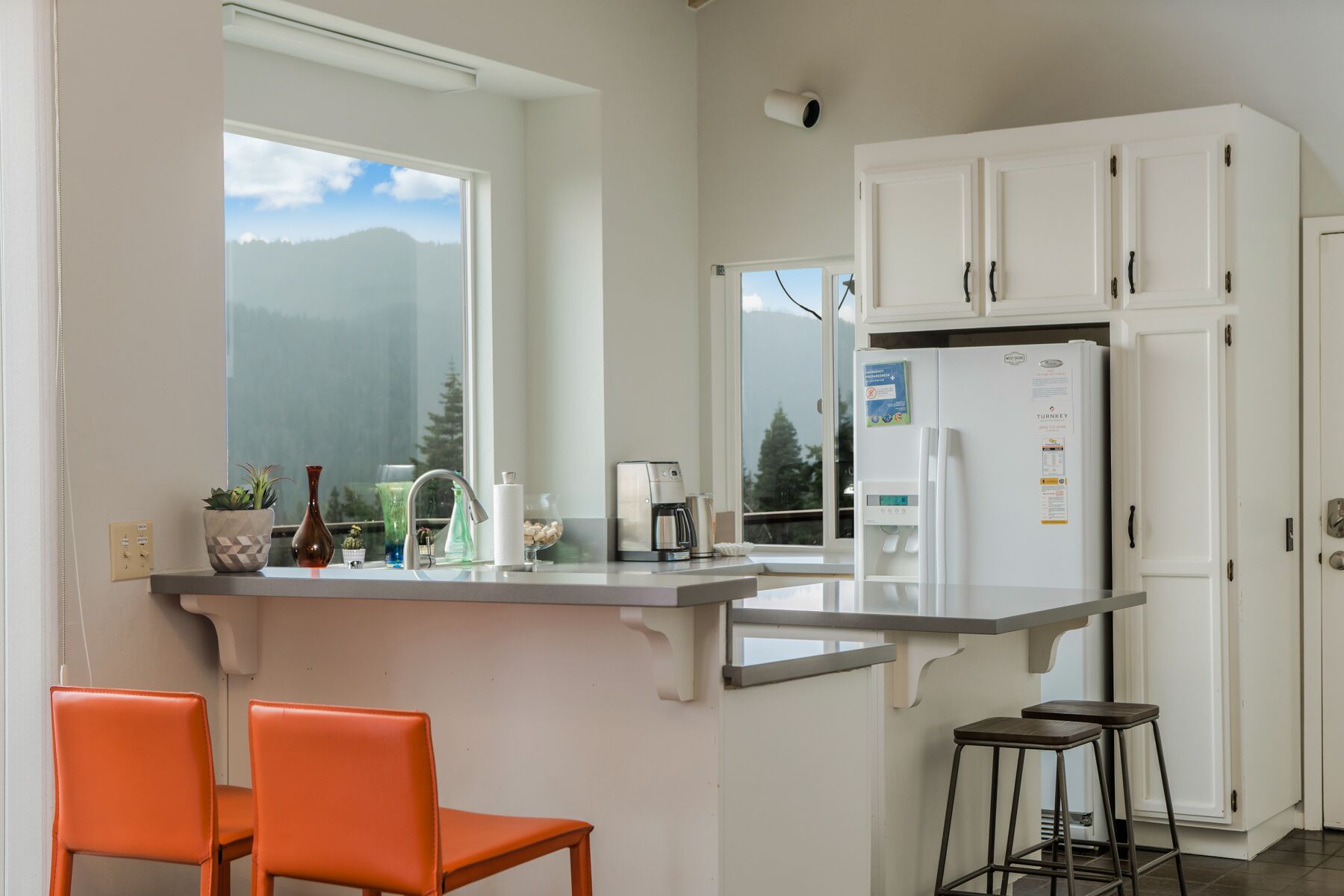 A kitchen with white cabinets, a built-in island with seating, a refrigerator, and a view of mountains through the window.