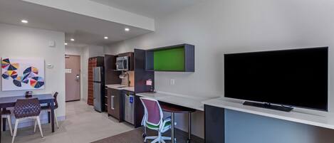 Uma sala de estar moderna com uma TV de tela plana, uma área de jantar com mesa e cadeiras, e uma cozinha com eletrodomésticos.