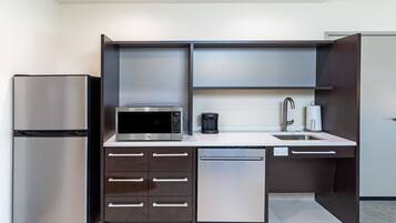 Eine kleine Küche mit Kühlschrank, Mikrowelle, Kaffeemaschine und Geschirrspüler.