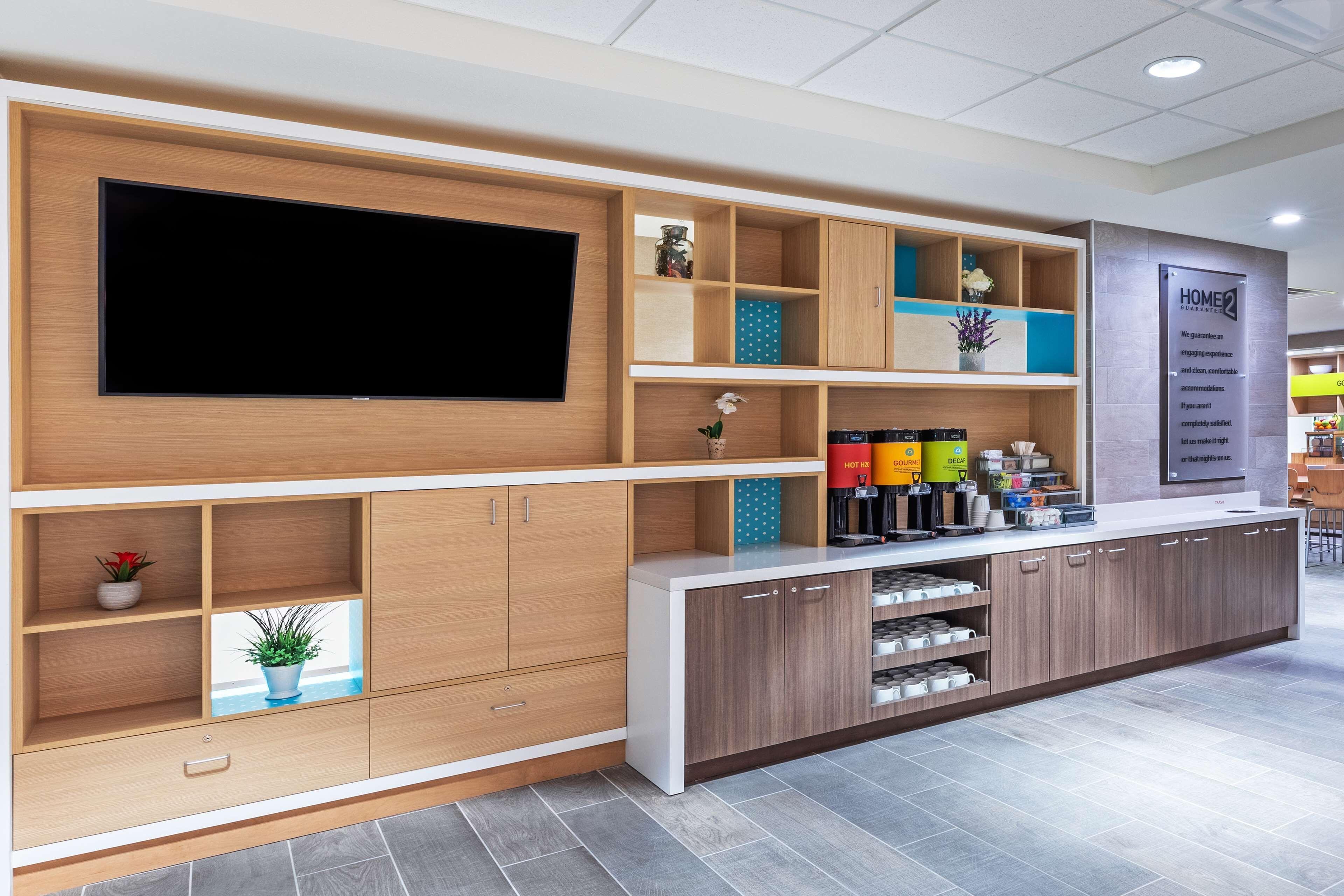 A modern kitchen with a large TV, wooden cabinets, and a coffee machine.
