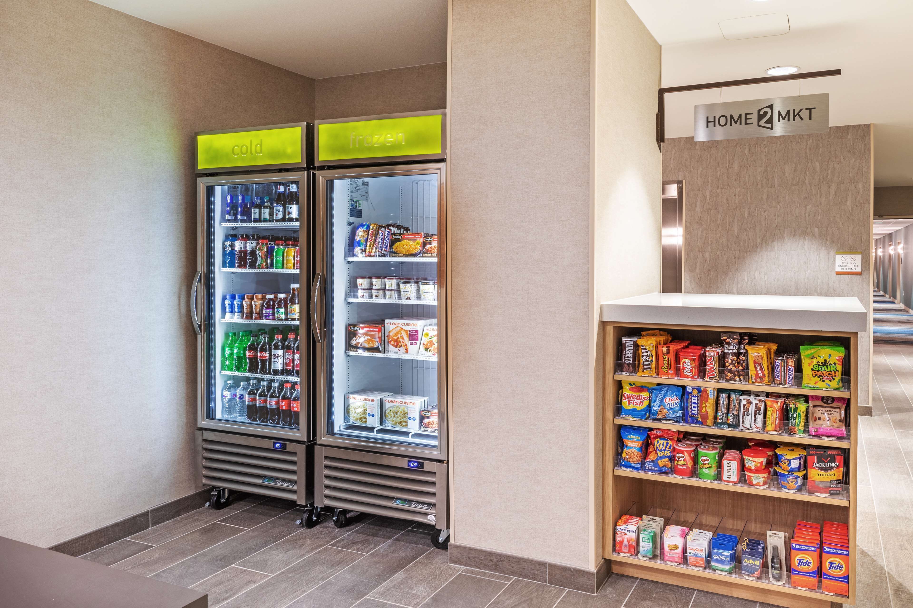 A hotel lobby with two beverage dispensers, a snack shelf, and a sign indicating the location.
