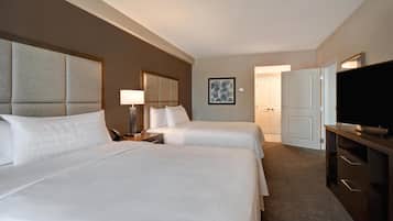 A hotel room with two beds, a TV, a desk with a lamp, and a door leading to another room.