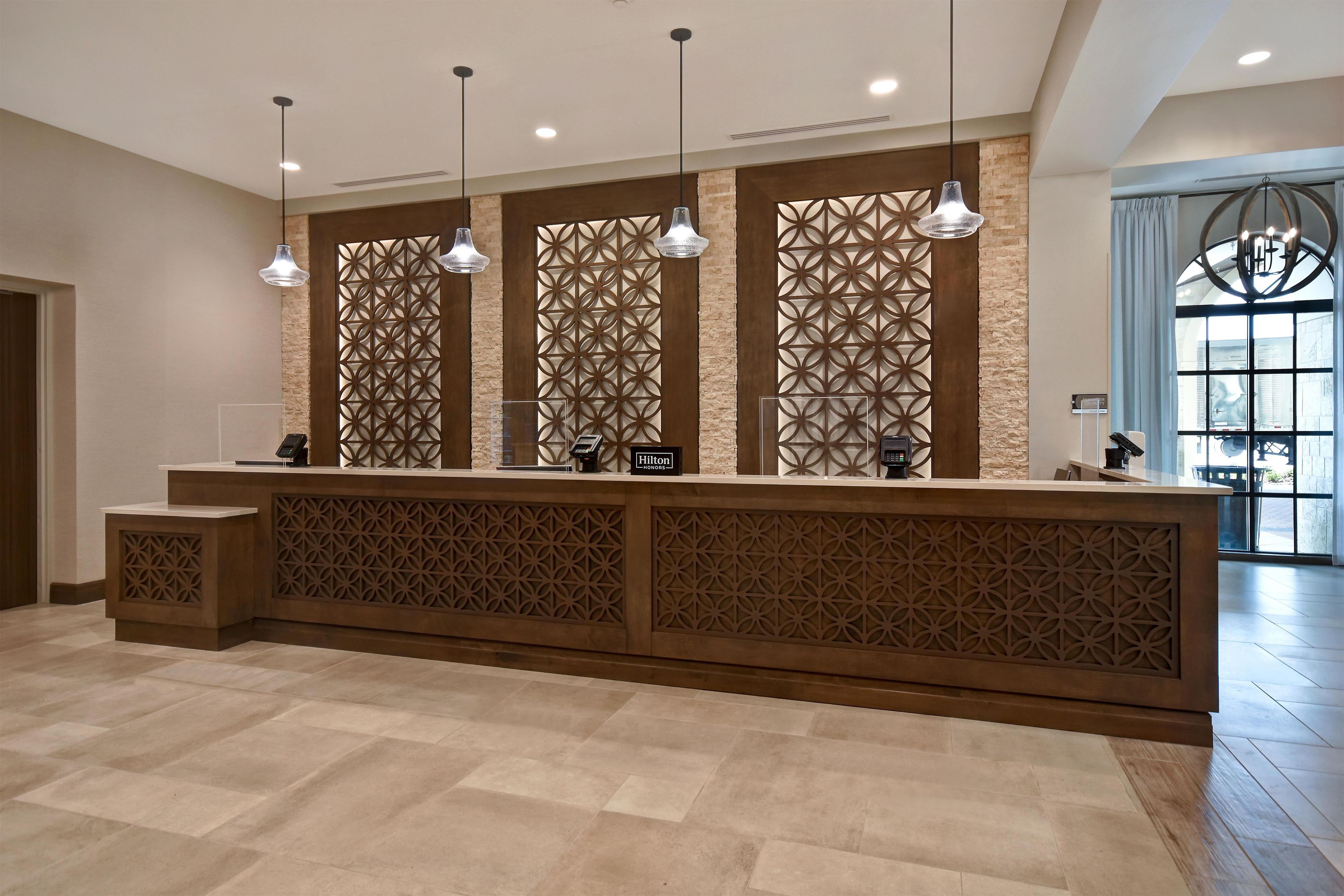 A hotel reception desk with a modern design, featuring geometric patterned panels, a flat surface for check-in, and pendant lighting.
