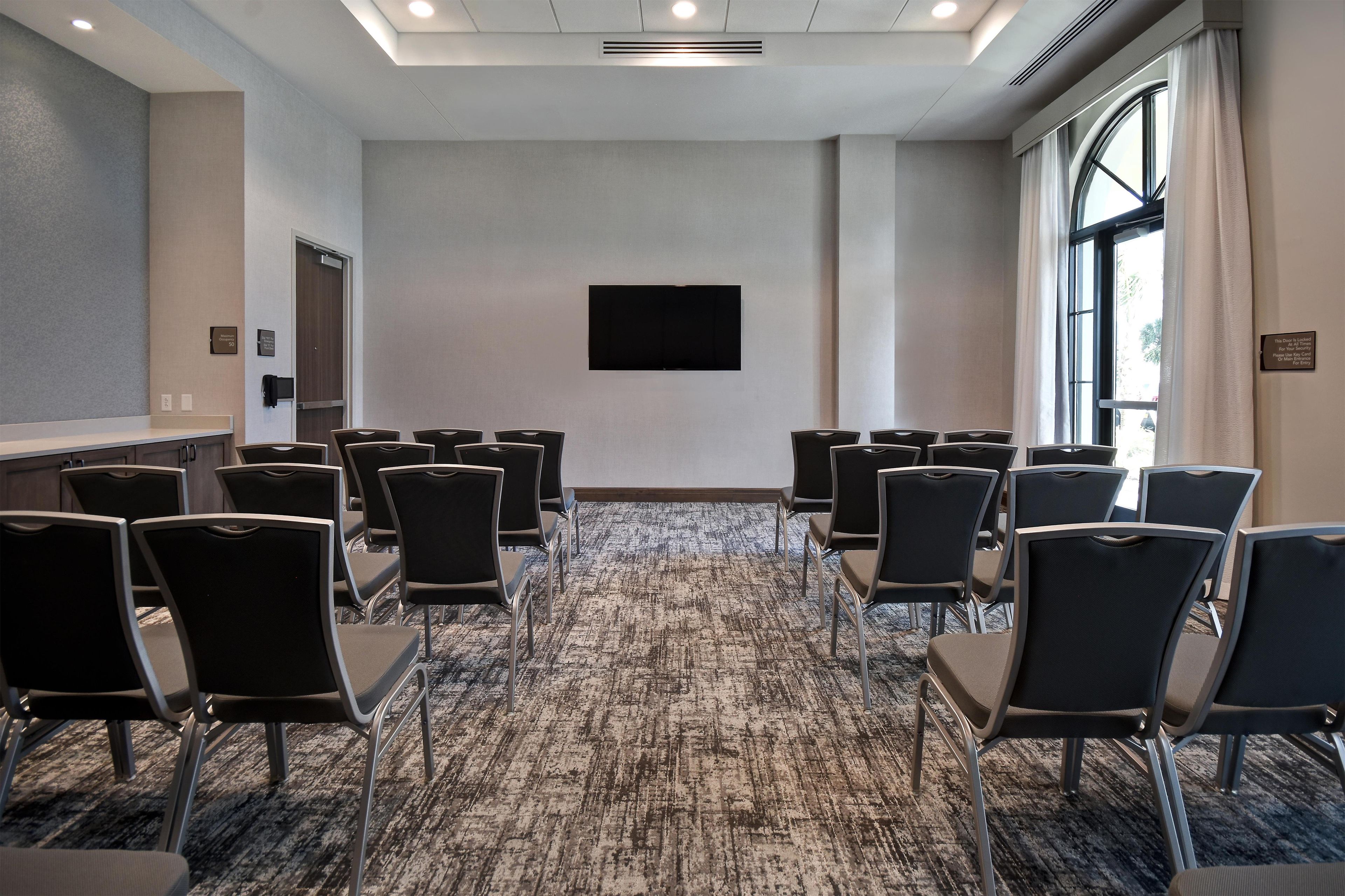 Ein Konferenzraum mit Reihen von Stühlen, einem Flachbildfernseher an der Wand und einem Teppichboden.