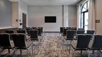 Une salle de conférence avec des rangées de chaises, un téléviseur à écran plat accroché au mur et un sol recouvert de moquette.