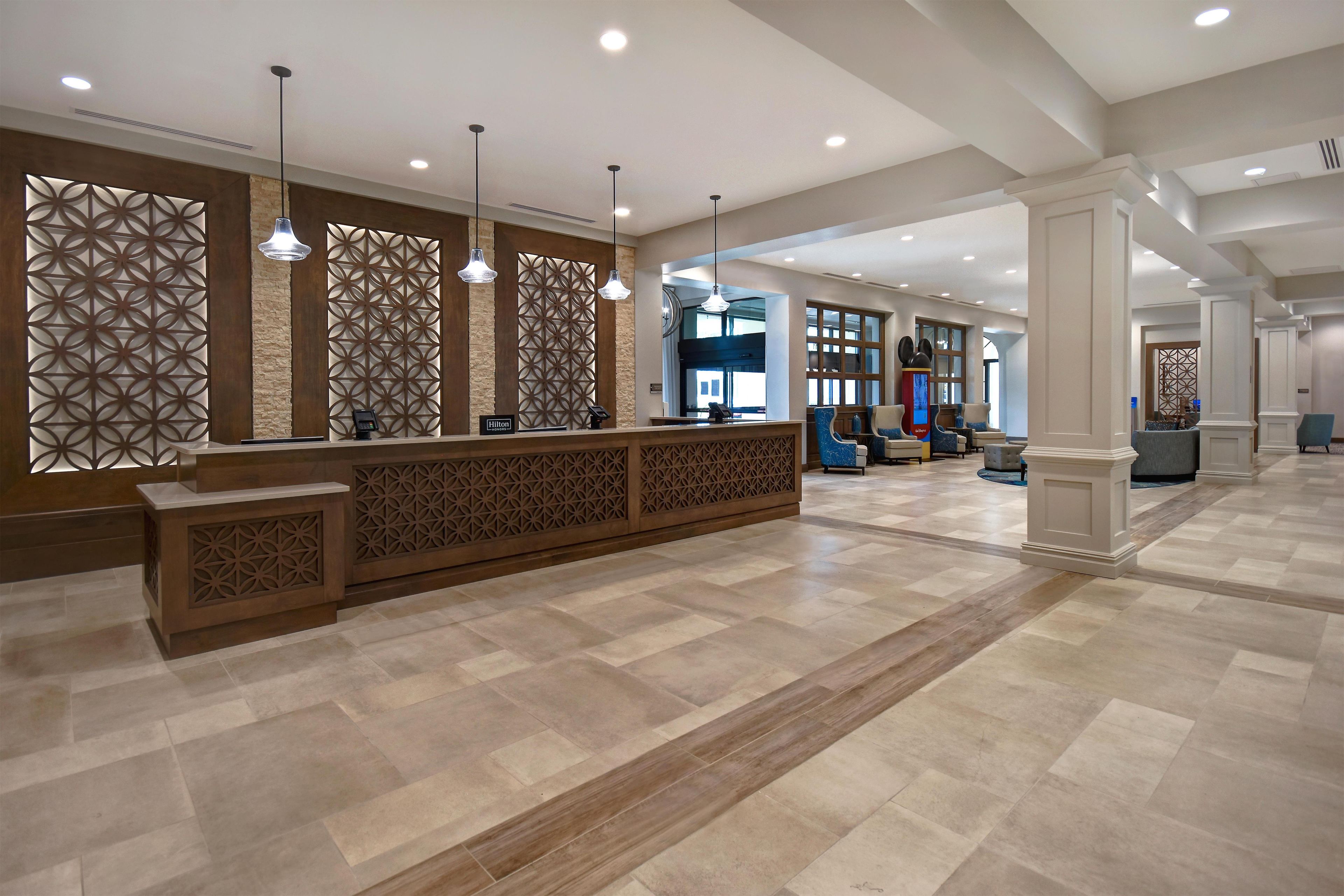A hotel reception area with a modern design, featuring a reception desk, seating area, and decorative panels.