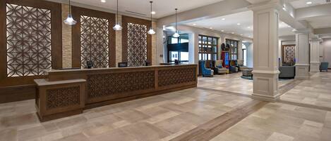 A hotel reception area with a modern design, featuring a reception desk, seating area, and decorative panels.