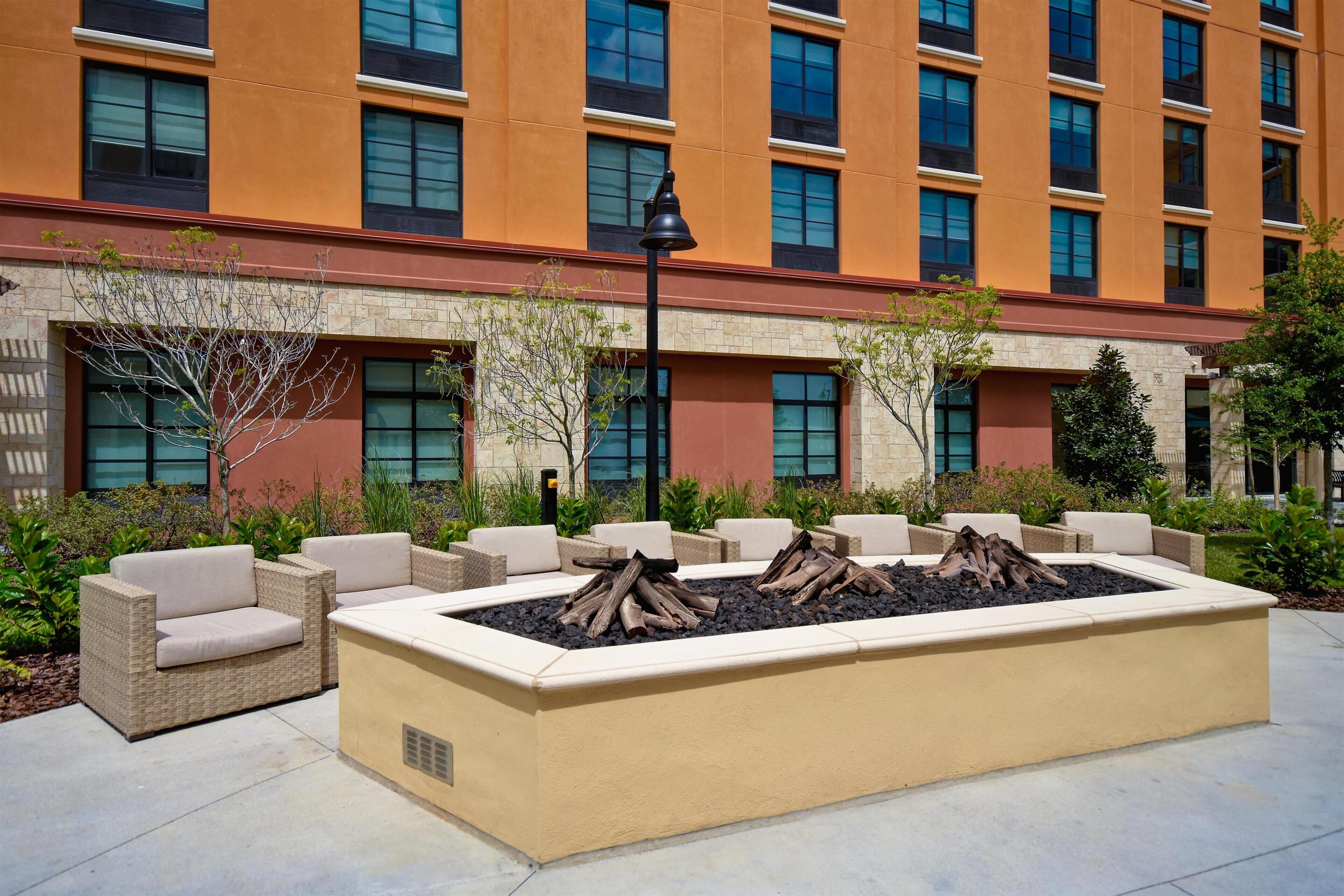 An outdoor seating area with a fire pit, wicker furniture, and a building with multiple windows in the background.