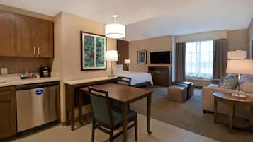 Une chambre d’hôtel équipée d’une kitchenette, d’un coin repas, d’un lit, d’une télévision et d’un espace détente avec un canapé et des fauteuils.