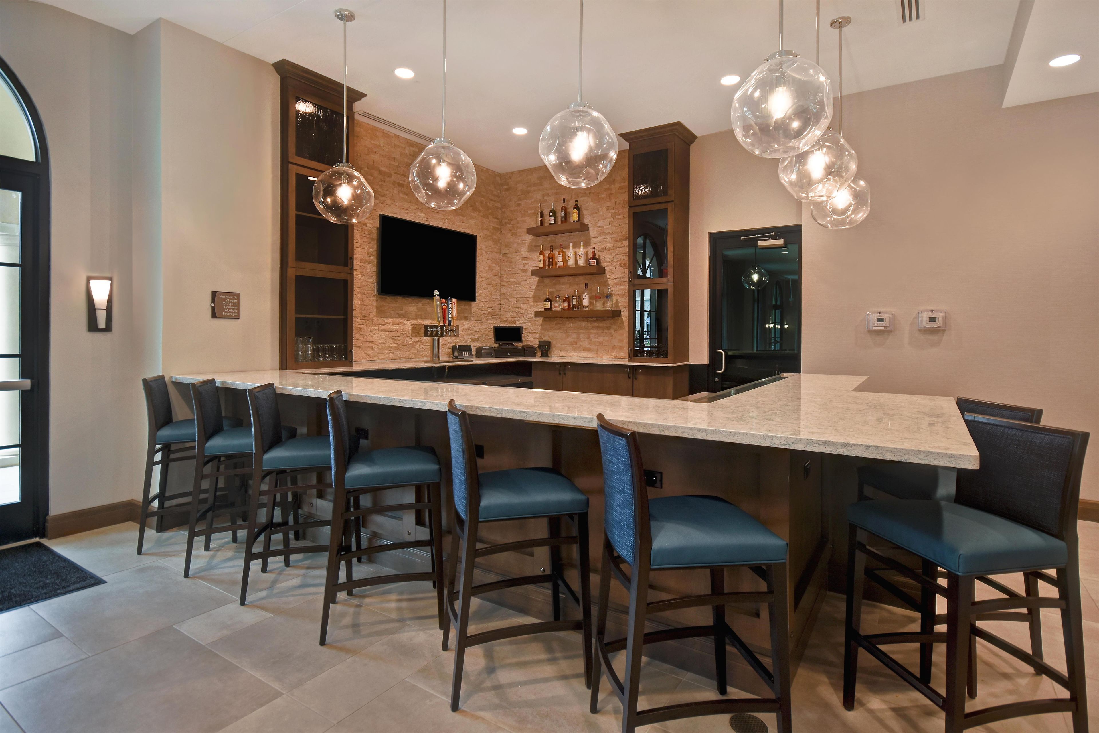 Una cocina moderna con barra, que cuenta con una isla grande con taburetes, iluminación colgante y un televisor de pantalla plana montado en una pared de ladrillo.