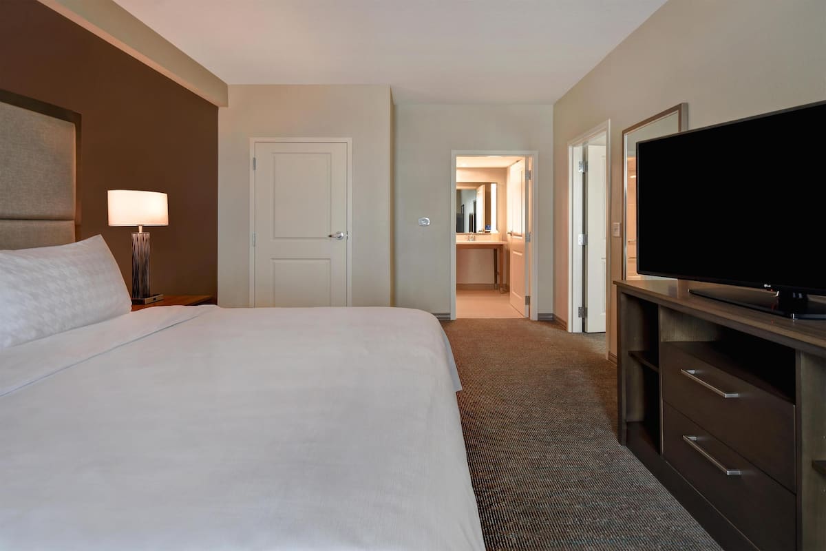 Een hotelkamer met een bed, een televisie, een lamp en een deur naar een badkamer.