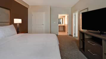 A hotel room with a bed, a TV, a lamp, and a door leading to a bathroom.