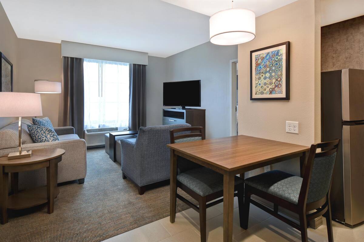 Een hotelkamer met een eettafel, stoelen, een bank, een televisie en een koelkast.