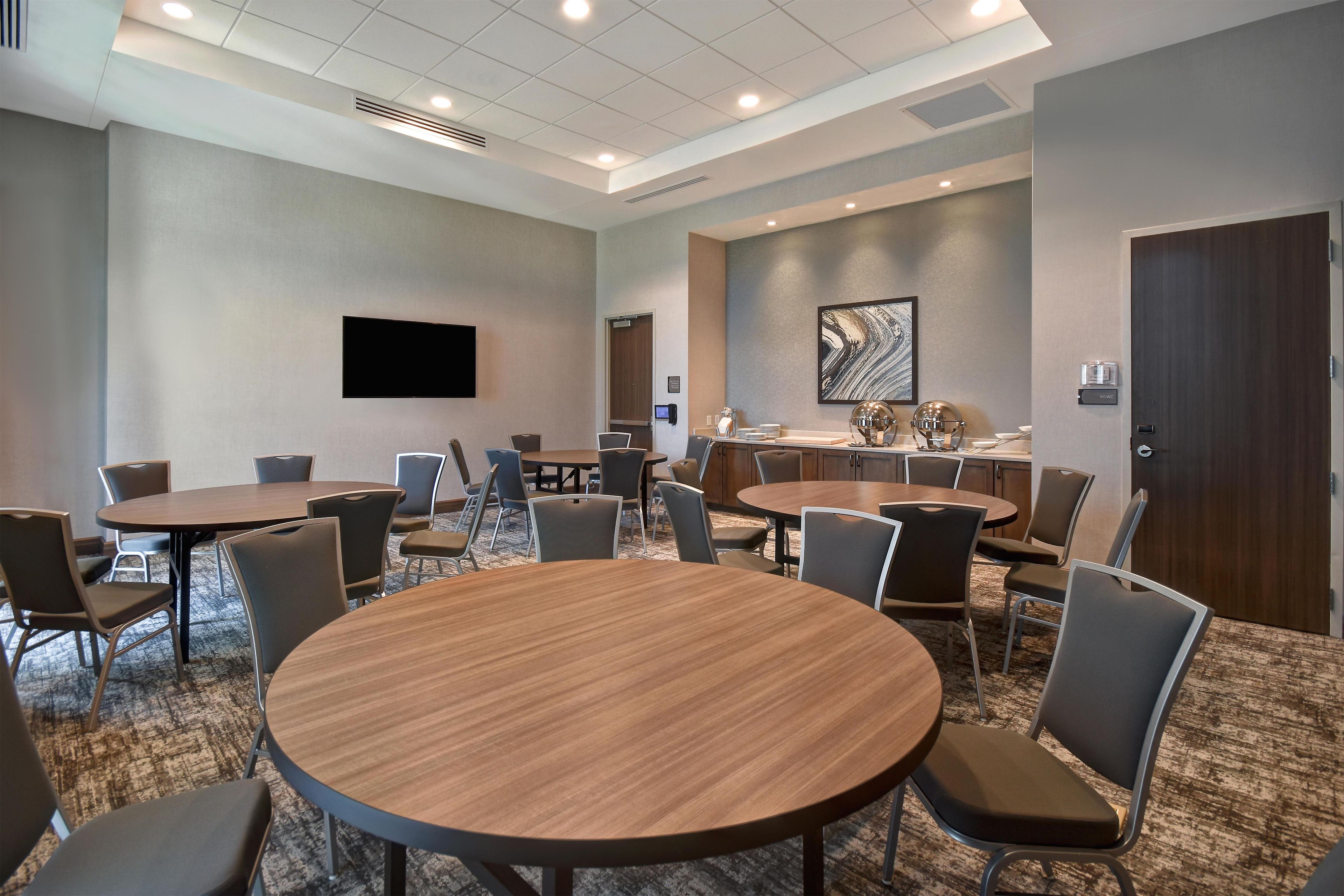 A conference room with multiple tables and chairs, a flat-screen TV mounted on the wall, and a large abstract painting.