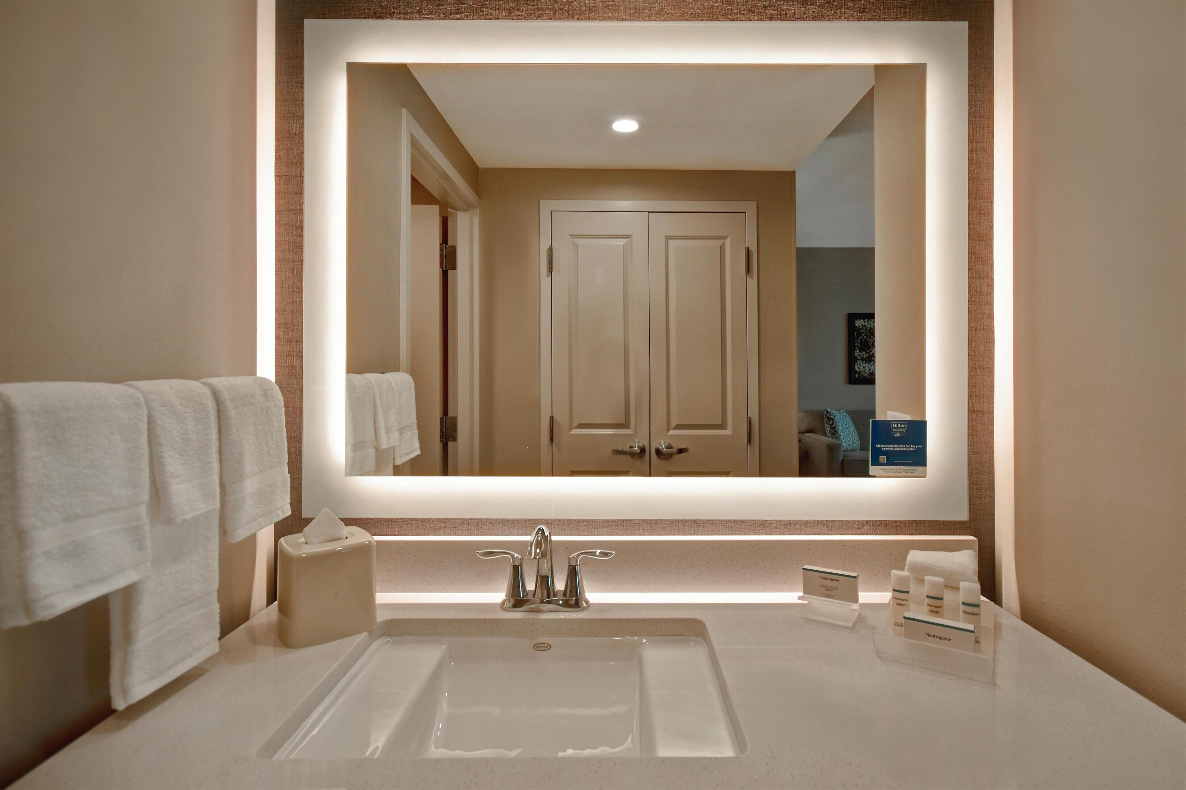 A bathroom with a large mirror, a sink, and a towel rack.