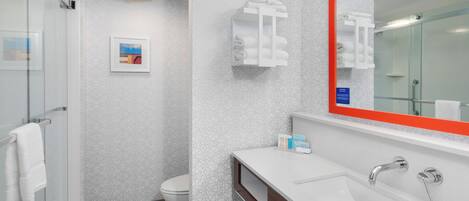 Un baño moderno con cabina de ducha de vidrio, inodoro blanco y tocador con espejo y lavamanos.