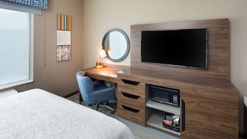 Habitación de hotel con cama, escritorio con silla, televisión, espejo y obras de arte en la pared.