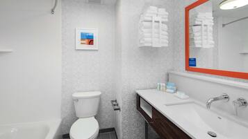 Une salle de bain moderne avec des toilettes, une baignoire et un lavabo. Un tableau encadré est accroché au mur et des serviettes sont disposées sur un porte-serviettes.