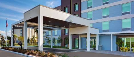 A modern hotel with a covered entrance, multiple floors, and a landscaped area with plants and outdoor seating.