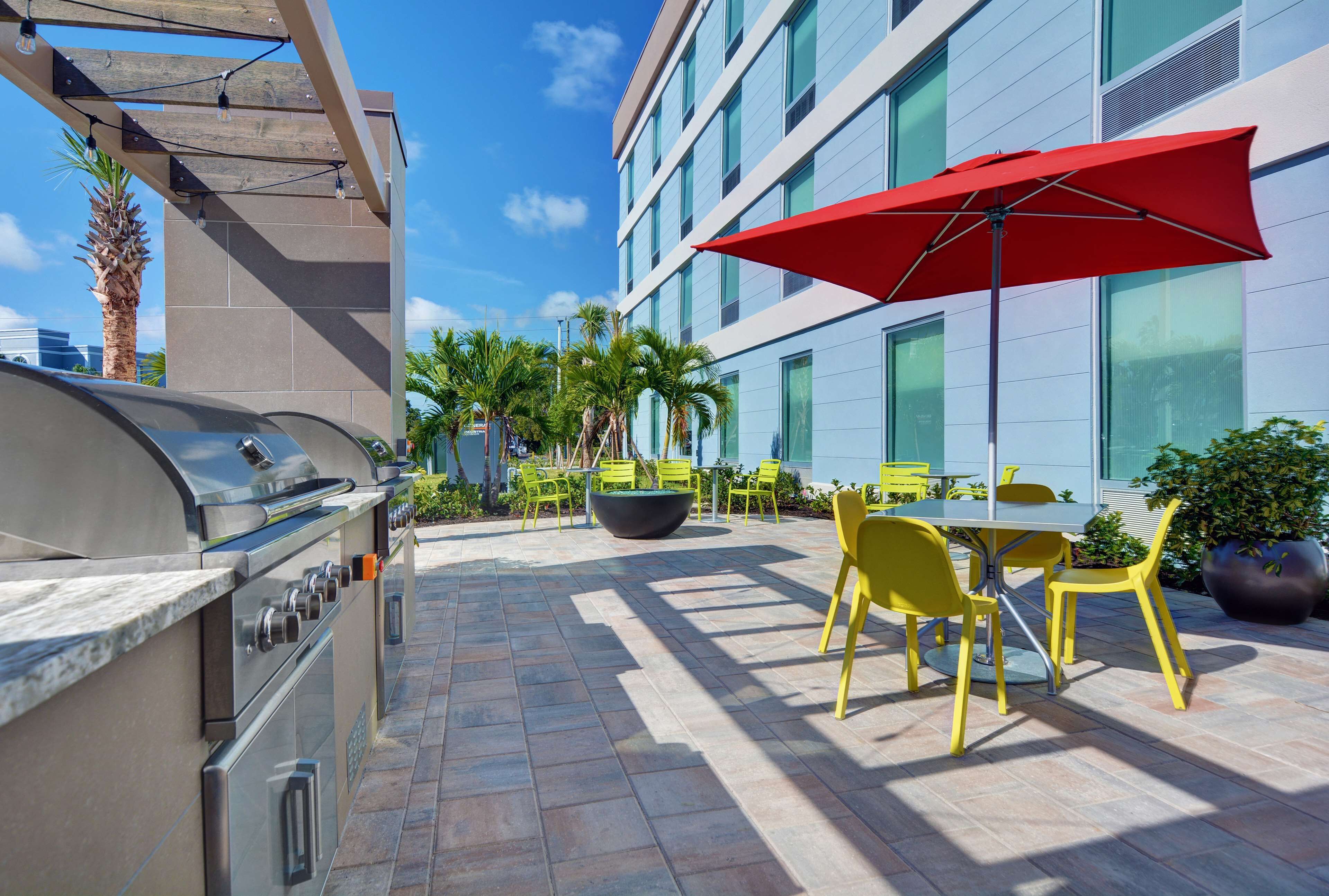 An outdoor patio with a barbecue grill, yellow chairs, and a red umbrella.