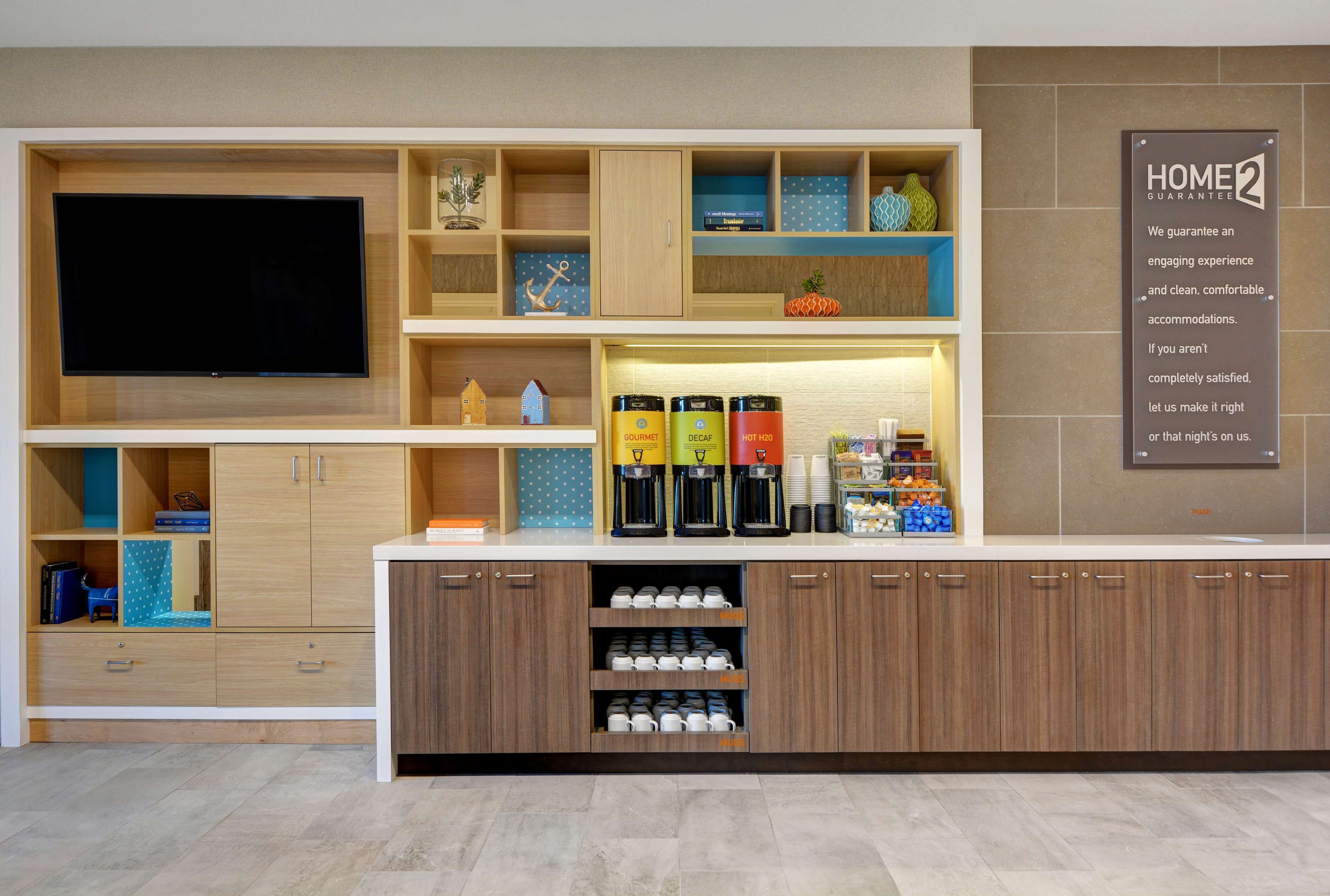 Un espace d’accueil d’hôtel équipé d’un téléviseur à écran plat, de meubles en bois et d’un coin café.