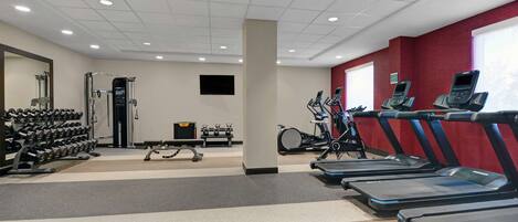 Un gimnasio con cintas de correr, mancuernas y máquinas de pesas.