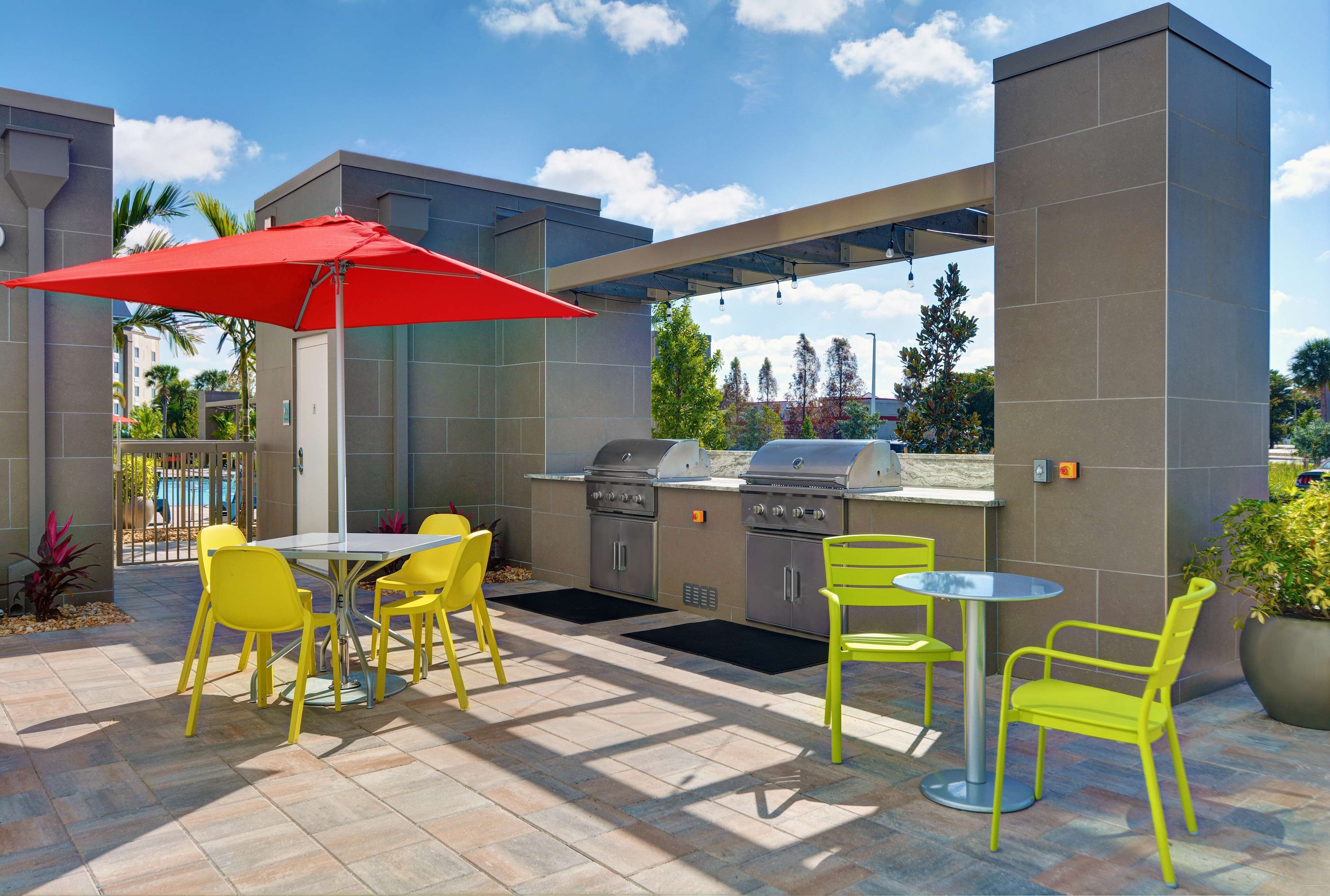 An outdoor patio with yellow chairs, a red umbrella, and a built-in grill station.