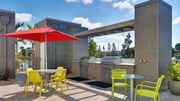 An outdoor patio with yellow chairs, a red umbrella, and a built-in grill station.