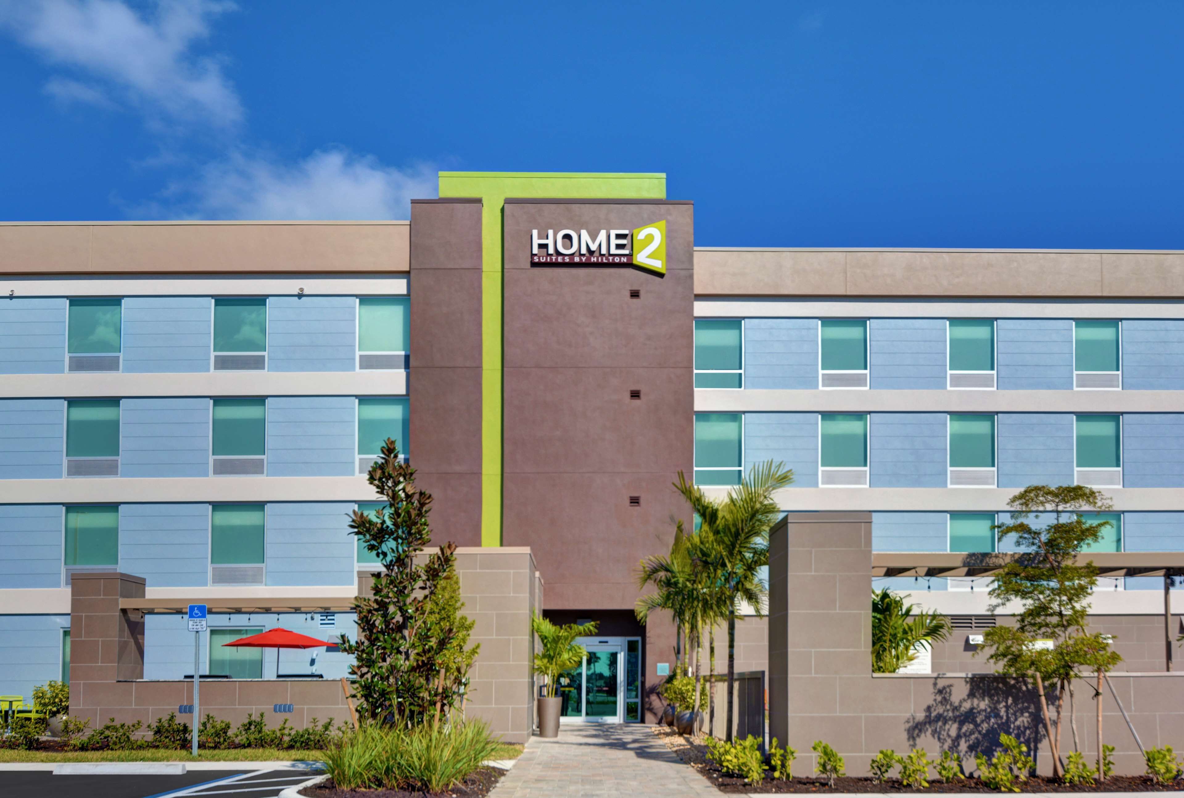 A modern hotel building with a sign reading "HOME 2 Suites by Hilton."