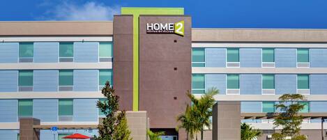 A modern hotel building with a sign reading "HOME 2 Suites by Hilton."