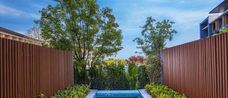 A rectangular swimming pool with a tiled edge, surrounded by lush greenery and wooden fences.