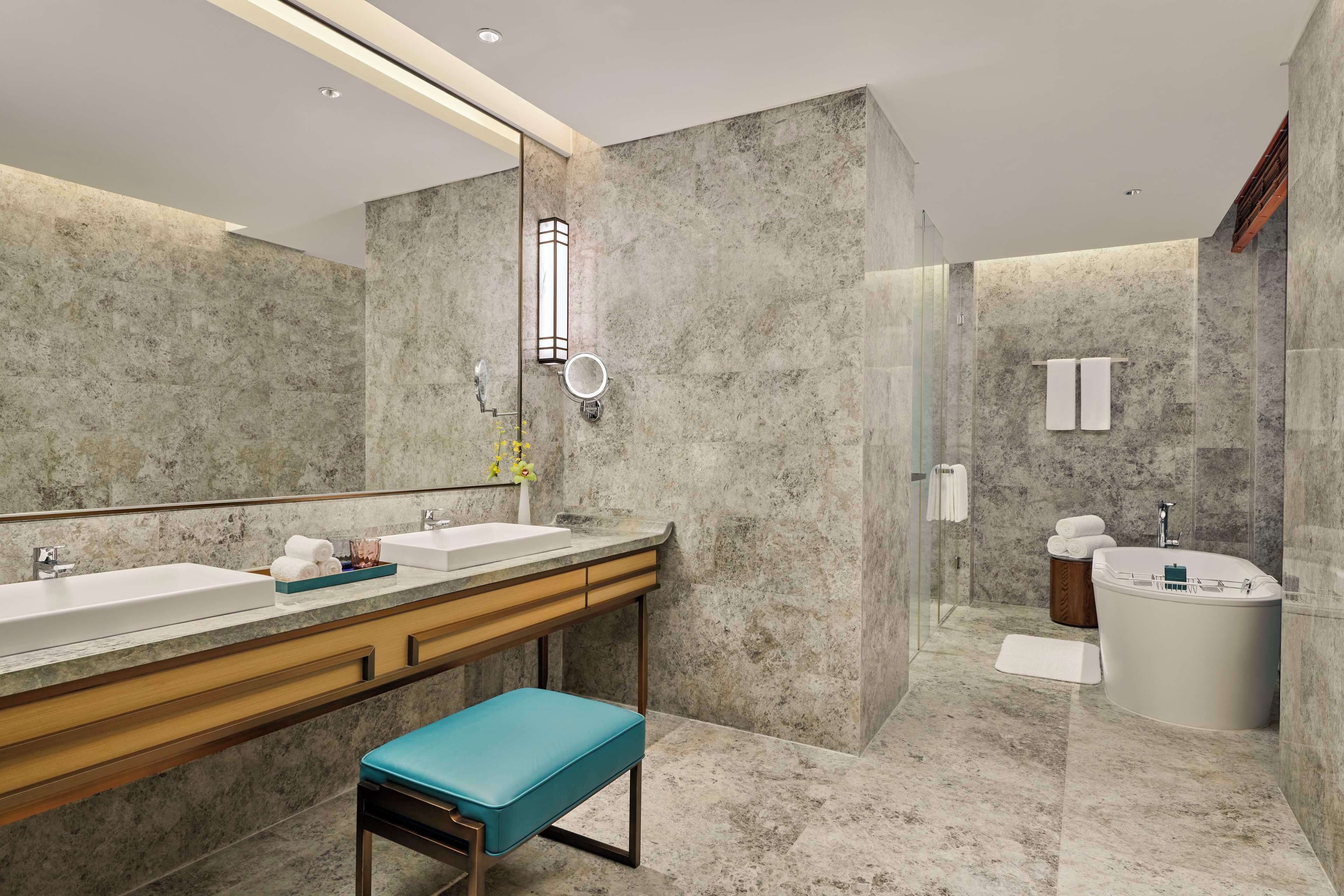 A modern bathroom with two sinks, a bathtub, a bench, and a large mirror.